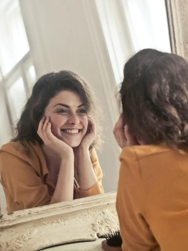 Mulher sorrindo diante do espelho em momento de conexão e autoconhecimento.