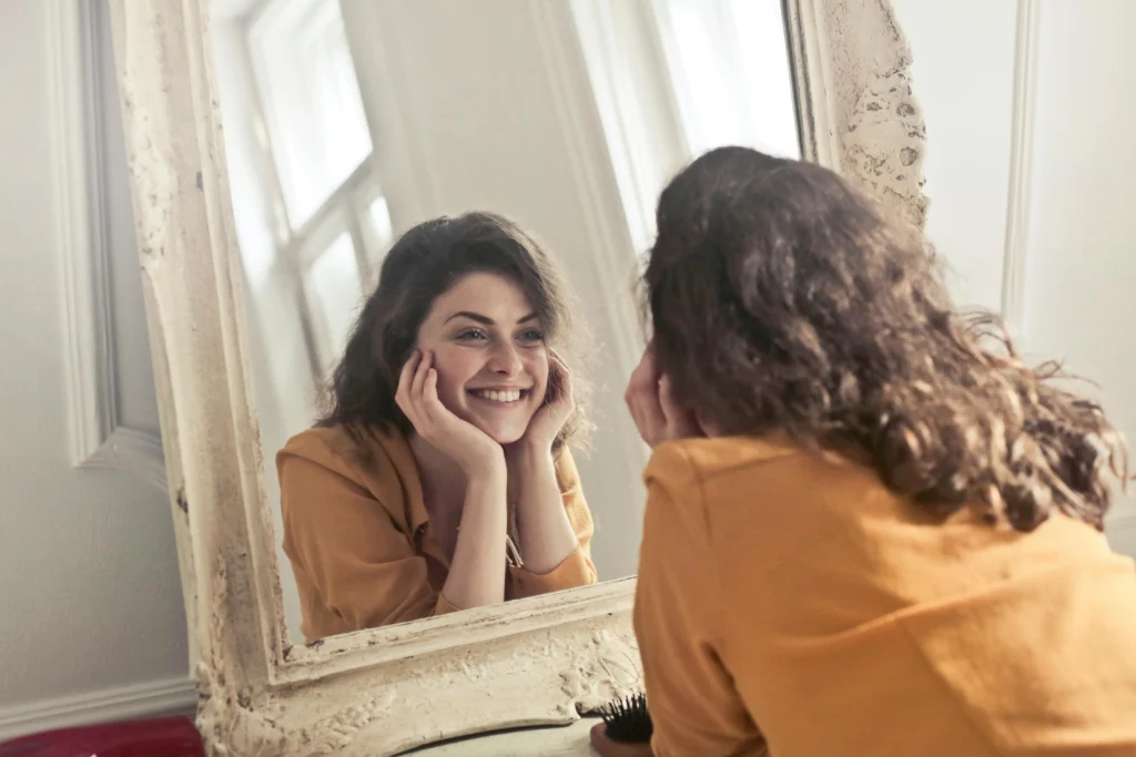 Mulher sorrindo diante do espelho em momento de conexão e autoconhecimento.