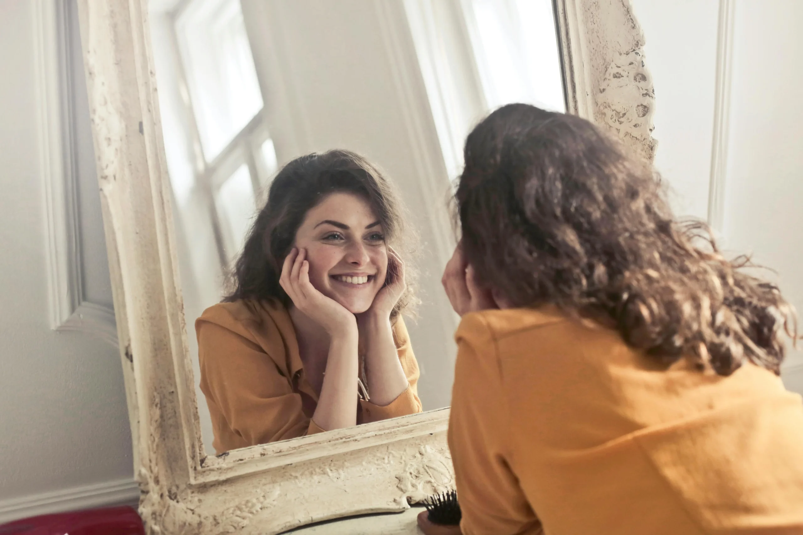 Mulher sorrindo diante do espelho em momento de conexão e autoconhecimento.
